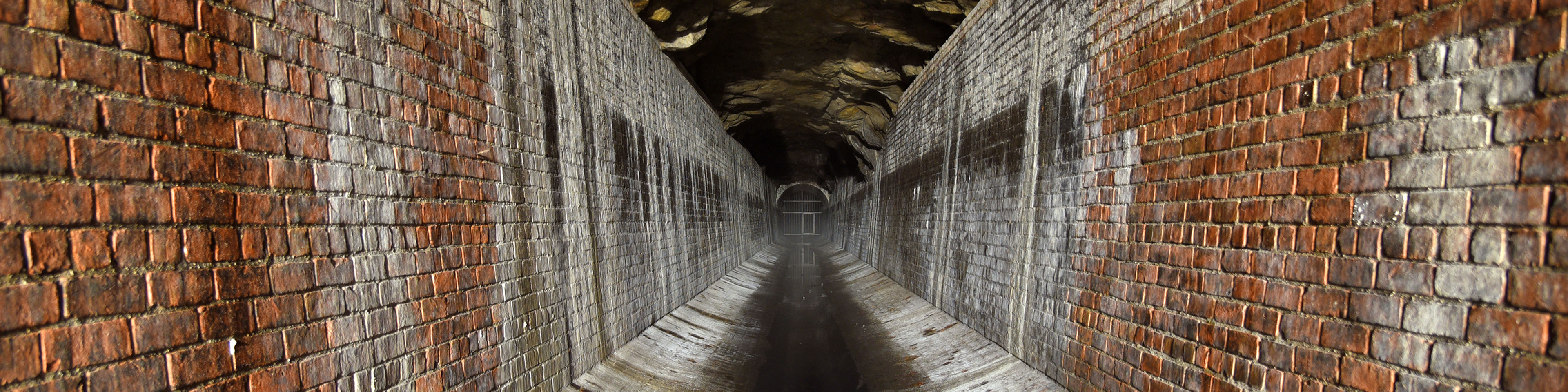 Inside a historic brick-lined tunnel receding toward a bright, arched opening in the distance